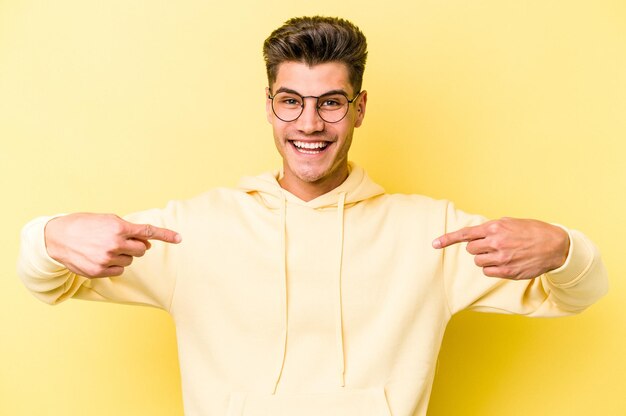 Jonge blanke man geïsoleerd op gele achtergrond wijst naar beneden met vingers positief gevoel