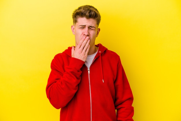 Jonge blanke man geïsoleerd op gele muur geeuwen met een moe gebaar dat mond bedekt met hand.