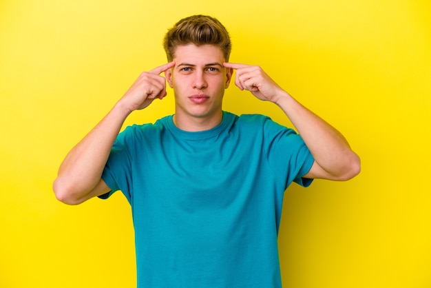 Jonge blanke man geïsoleerd op gele muur gericht op een taak, met wijsvingers wijzend hoofd.