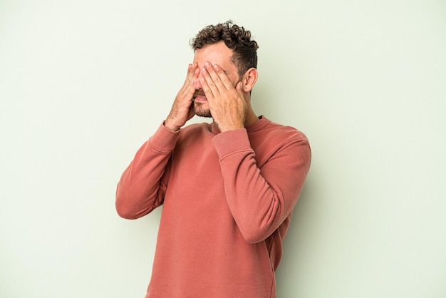 Jonge blanke man geïsoleerd op groene achtergrond bang voor ogen met handen.