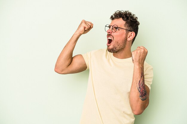 Jonge blanke man geïsoleerd op groene achtergrond die vuist opheft na een overwinning, winnaar concept.