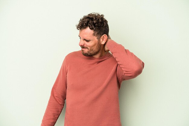 Jonge blanke man geïsoleerd op groene achtergrond met nekpijn als gevolg van stress, masseren en aanraken met de hand.