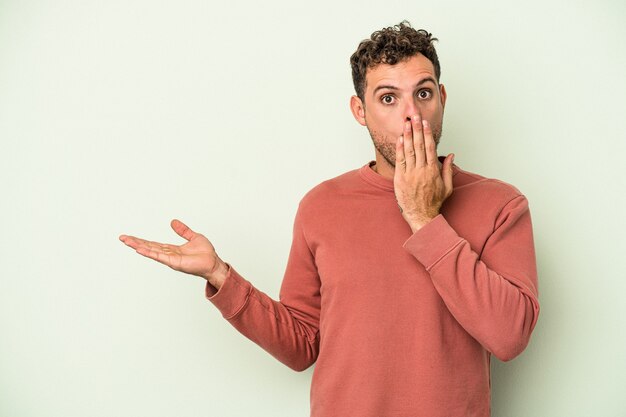 Jonge blanke man geïsoleerd op groene achtergrond onder de indruk met kopie ruimte op palm.