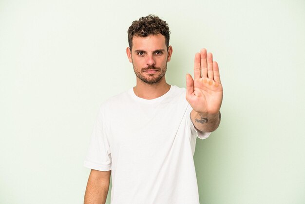 Jonge blanke man geïsoleerd op groene achtergrond permanent met uitgestrekte hand weergegeven: stopbord, voorkomen dat u.