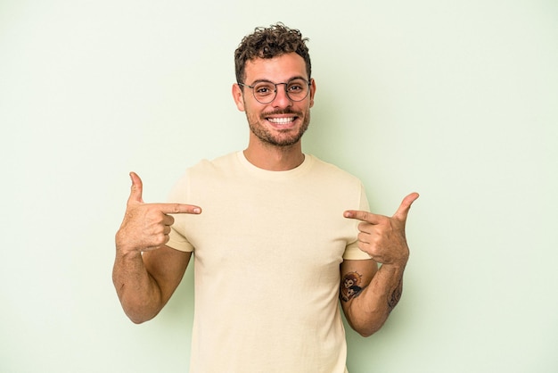 Jonge blanke man geïsoleerd op groene achtergrond wijst naar beneden met vingers, positief gevoel.