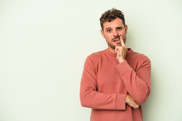 Jonge blanke man geïsoleerd op groene achtergrond zijwaarts kijkend met twijfelachtige en sceptische uitdrukking.