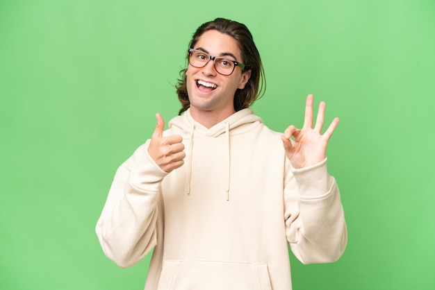 Jonge blanke man geïsoleerd op groene chroma achtergrond met ok teken en duim omhoog gebaar