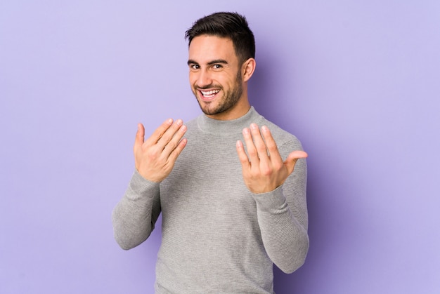 Jonge blanke man geïsoleerd op paars wijzend met de vinger naar je alsof uitnodigend dichterbij komen.