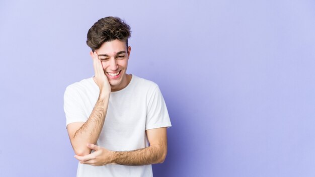 Jonge blanke man geïsoleerd op paarse ruimte lacht vrolijk en heeft plezier met handen op de buik.