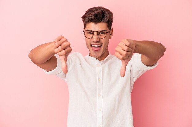 Jonge blanke man geïsoleerd op roze achtergrond duim omlaag tonen en afkeer uiten.