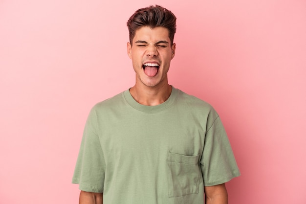 Jonge blanke man geïsoleerd op roze achtergrond grappig en vriendelijk tong uitsteekt.