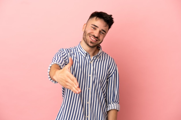 Jonge blanke man geïsoleerd op roze achtergrond handen schudden voor het sluiten van een goede deal