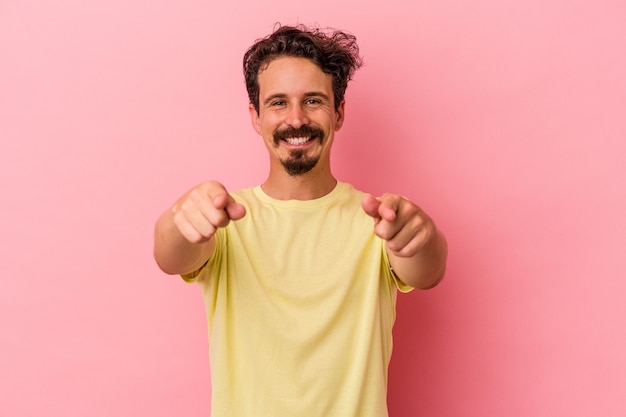 Jonge blanke man geïsoleerd op roze achtergrond vrolijke glimlach wijzend naar voren.