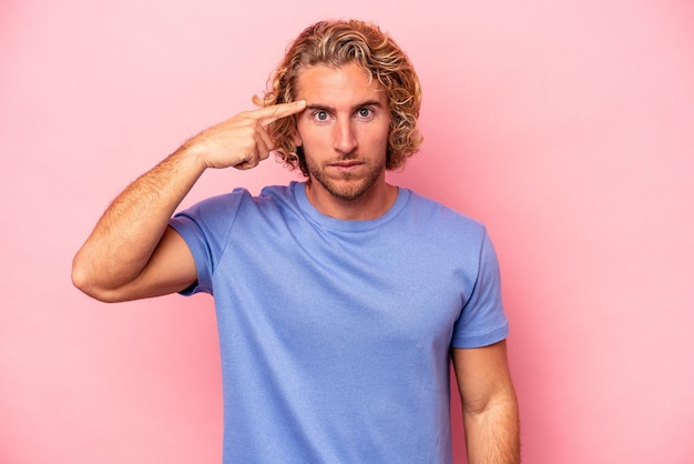 Jonge blanke man geïsoleerd op roze achtergrond wijzende tempel met vinger, denken, gericht op een taak.