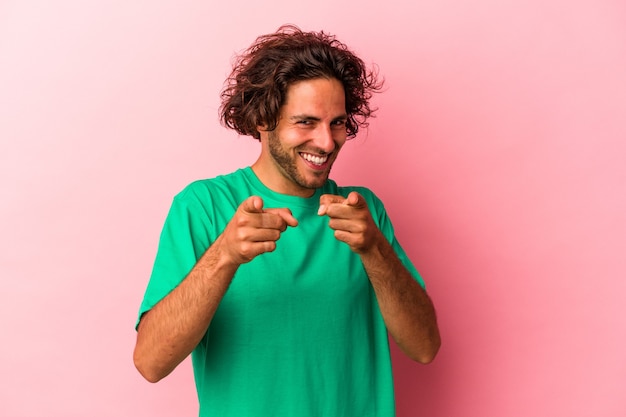 Jonge blanke man geïsoleerd op roze bakcground wijzend naar voren met vingers.