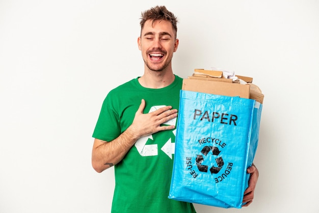 Jonge blanke man gerecycled papier geïsoleerd op een witte achtergrond lacht hardop met de hand op de borst.