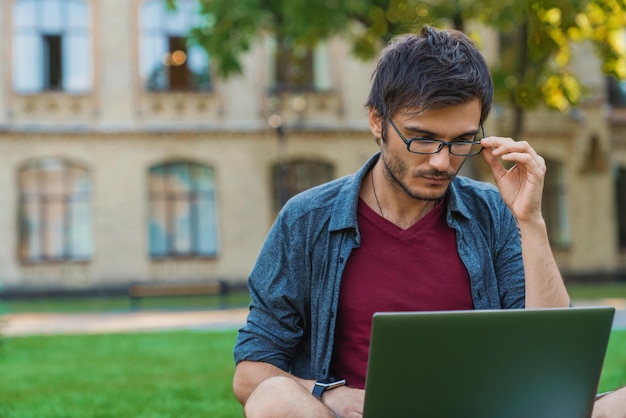 Jonge blanke man in bril met zijn laptop op het gras