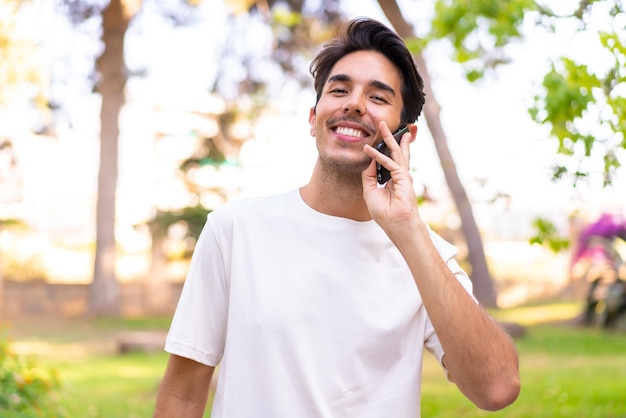 Jonge blanke man in een park die een gesprek voert met de mobiele telefoon met iemand