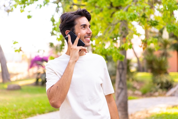 Jonge blanke man in een park die een gesprek voert met de mobiele telefoon met iemand