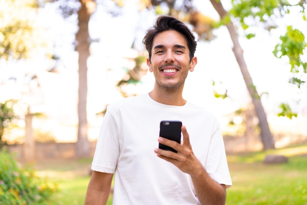 Jonge blanke man in een park met behulp van mobiele telefoon