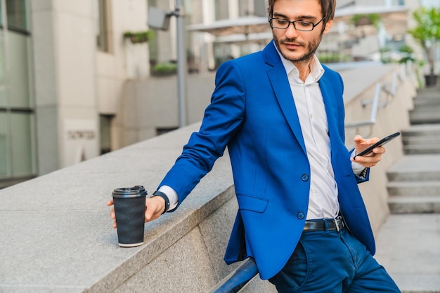 Jonge blanke man in formalwear die een koffiekopje neemt terwijl hij pauze heeft in de straat van de stad