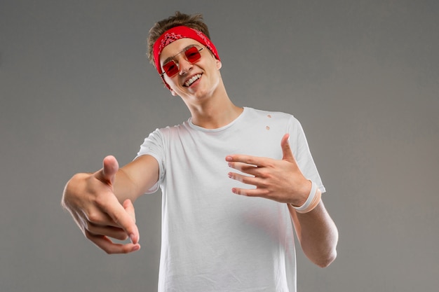 Jonge blanke man in rode zonnebril, witte t-shirt poseren geïsoleerd op grijze muur