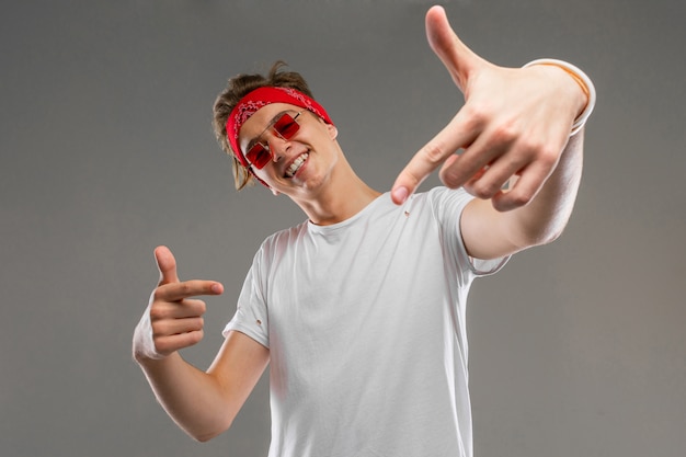 Jonge blanke man in rode zonnebril, witte t-shirt poseren geïsoleerd op grijze muur