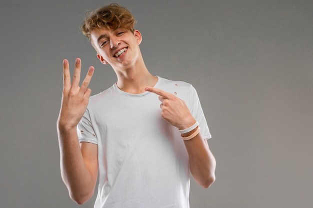 Jonge blanke man in wit t-shirt poseren en gebaren geïsoleerd op grijze muur