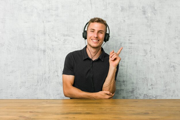 Jonge blanke man luisteren naar muziek met koptelefoon glimlachen vrolijk wijzend met wijsvinger weg.