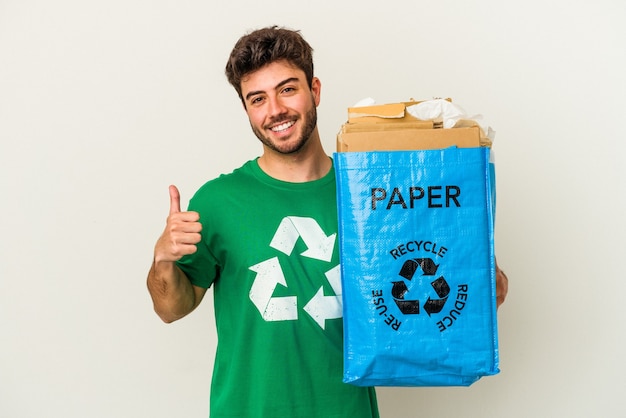 Jonge blanke man man recycling karton geïsoleerd op een witte achtergrond glimlachend en duim omhoog