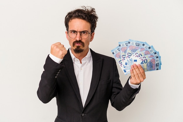 Jonge blanke man met bankbiljetten geïsoleerd op een witte achtergrond met vuist naar camera, agressieve gezichtsuitdrukking.