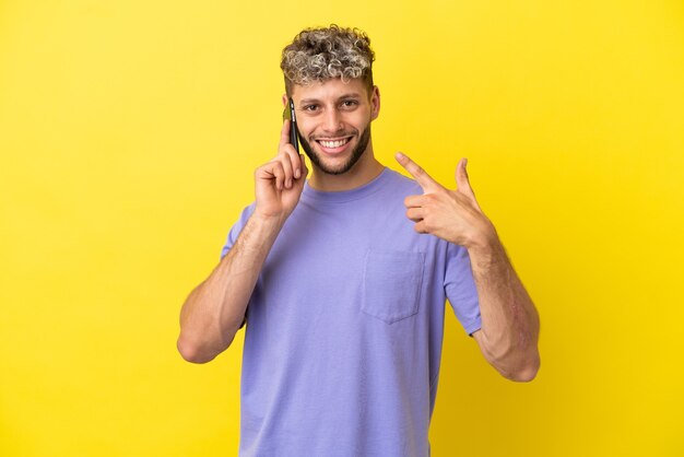 Jonge blanke man met behulp van mobiele telefoon geïsoleerd op gele achtergrond met een duim omhoog gebaar