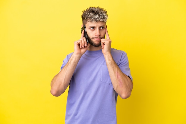 Jonge blanke man met behulp van mobiele telefoon geïsoleerd op gele achtergrond met twijfels en denken