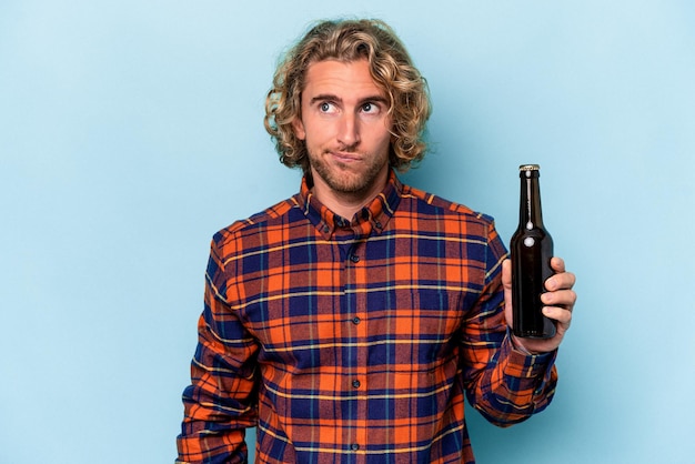 Foto jonge blanke man met bier geïsoleerd op een witte achtergrond verward, voelt zich twijfelachtig en onzeker.
