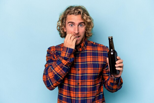 Jonge blanke man met bier geïsoleerd op een witte achtergrond vingernagels bijten, nerveus en erg angstig.