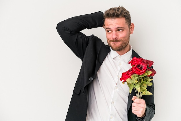 Jonge blanke man met boeket bloemen geïsoleerd op een witte achtergrond achterhoofd aanraken, denken en een keuze maken.