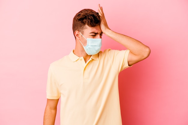 Jonge blanke man met een bescherming tegen coronavirus geïsoleerd op roze muur iets vergeten, voorhoofd slaan met handpalm en ogen sluiten.