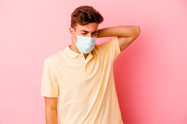 Jonge blanke man met een bescherming voor coronavirus geïsoleerd op een roze achtergrond met nekpijn als gevolg van een zittende levensstijl.