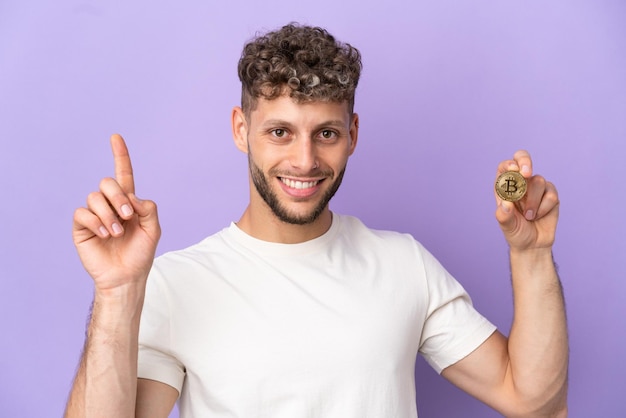 Jonge blanke man met een Bitcoin geïsoleerd op een paarse achtergrond die een geweldig idee benadrukt