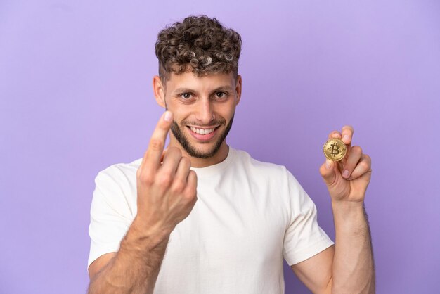 Jonge blanke man met een Bitcoin geïsoleerd op een paarse achtergrond die een komend gebaar doet