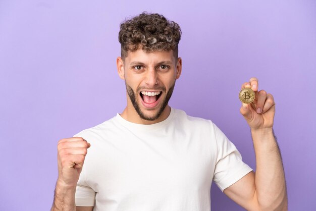 Jonge blanke man met een Bitcoin geïsoleerd op een paarse achtergrond die een overwinning viert in winnaarspositie