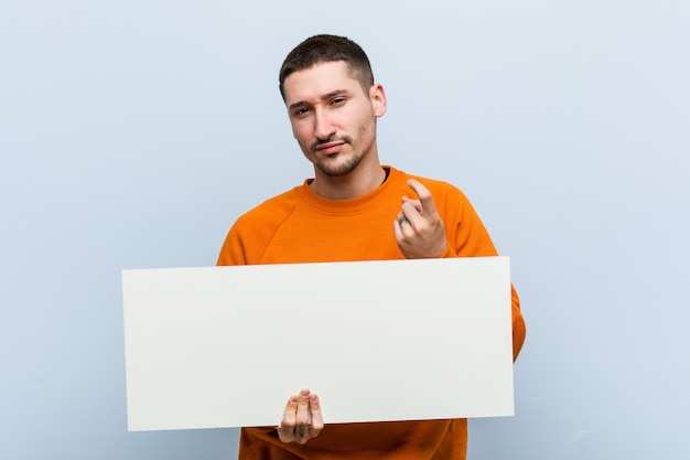 Jonge blanke man met een bordje wijzend met de vinger naar je alsof uitnodigen dichterbij komen.