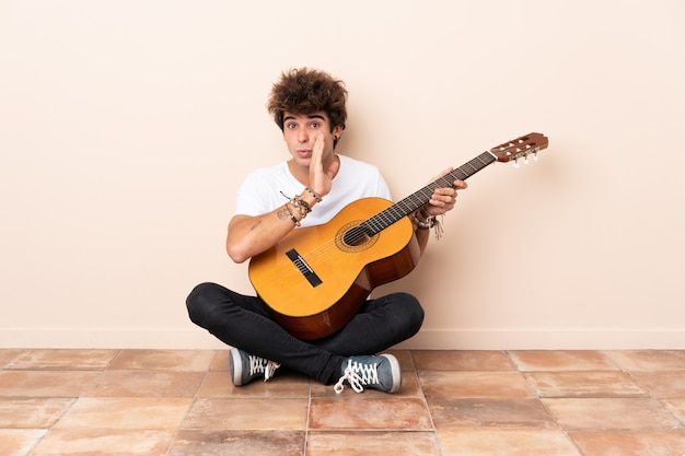 Jonge blanke man met een gitaar zittend op de vloer iets fluisteren