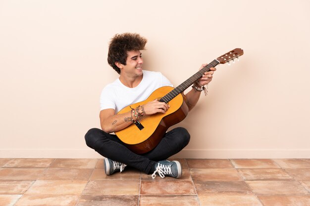 Jonge blanke man met een gitaar zittend op de vloer met gelukkige uitdrukking