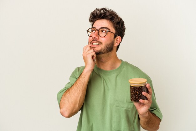 Jonge blanke man met een koffiepot geïsoleerd op een witte achtergrond ontspannen denken over iets kijken naar een kopie ruimte.