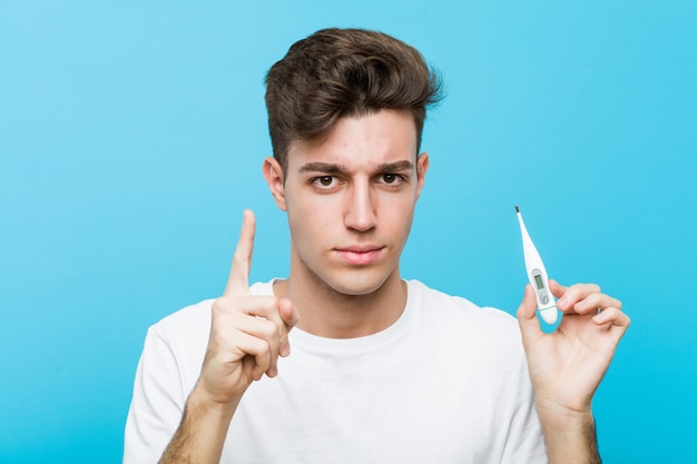 Jonge blanke man met een medische thermometer met nummer één met vinger.