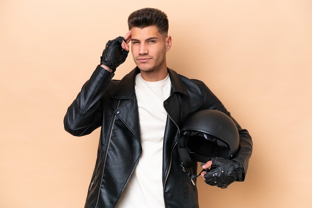 Jonge blanke man met een motorhelm geïsoleerd op beige achtergrond met twijfels en denken