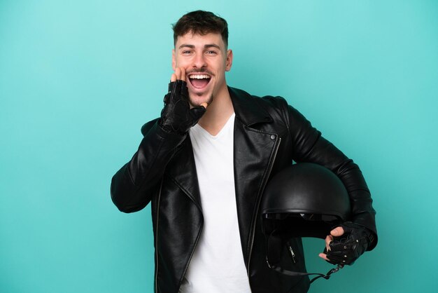 Jonge blanke man met een motorhelm geïsoleerd op blauwe achtergrond schreeuwen met wijd open mond