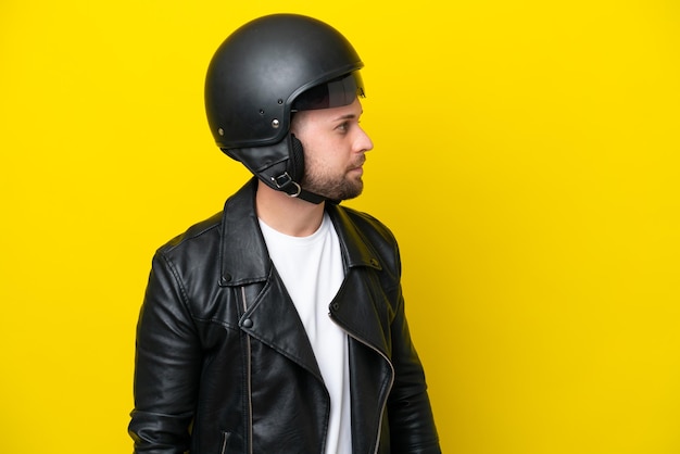 Jonge blanke man met een motorhelm geïsoleerd op een gele achtergrond op zoek naar de zijkant