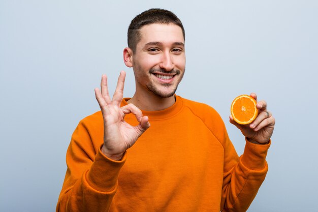 Jonge blanke man met een oranje vrolijk en zelfverzekerd weergegeven: ok gebaar.